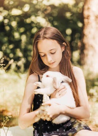 A little girl holds a white rabbit in her arms in nature in the summerの写真素材