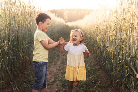 A boy and girl brother and sister play in the field in the summer. Happy summer vacation. Boy and girl on country road. Wheat fieldの写真素材
