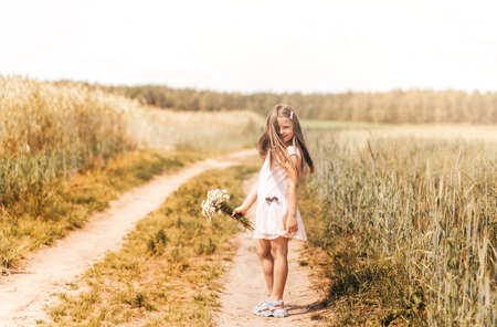 A little blonde girl walks through a golden field in the summer. Concept of purity, growth, happinessの写真素材