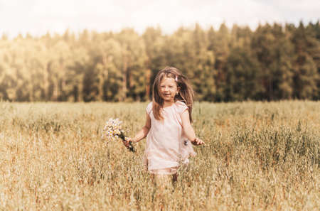 A little blonde girl walks through a golden field in the summer. Concept of purity, growth, happinessの写真素材