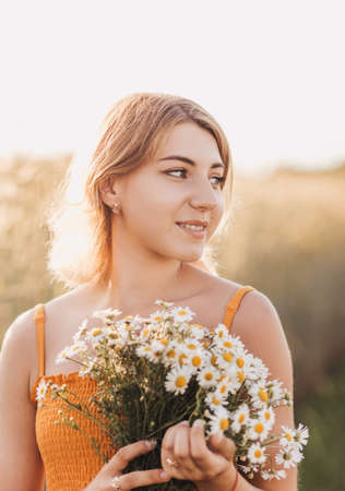 Young beautiful girl with a bouquet of daisies in a wheat fieldの写真素材