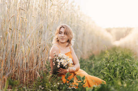 Young beautiful girl with a bouquet of daisies in a wheat fieldの写真素材