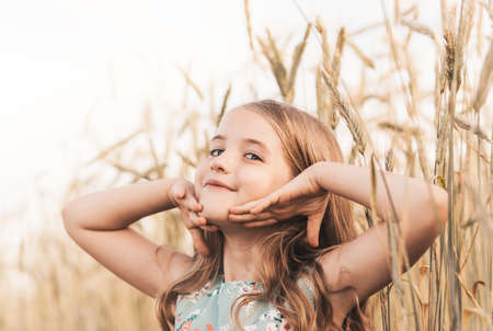 A happy little girl runs through a wheat field in the summer on a sunny day. Summertime. Summer vacation. Happy childhood. Positive emotions and energyの写真素材