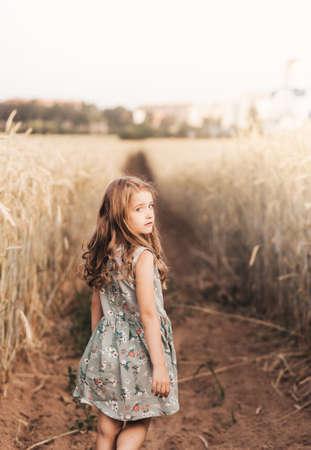 A happy little girl runs through a wheat field in the summer on a sunny day. Summertime. Summer vacation. Happy childhood. Positive emotions and energyの写真素材