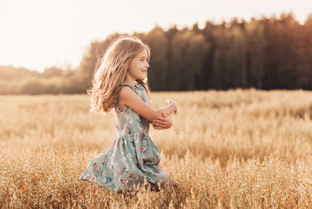 A happy little girl runs through a wheat field in the summer on a sunny day. Summertime. Summer vacation. Happy childhood. Positive emotions and energyの写真素材