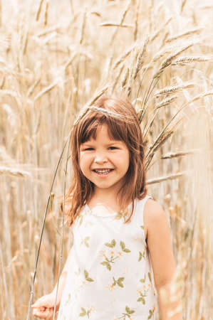 A little girl plays with spikelets in a wheat fieldの写真素材