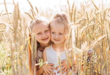 Older sister kisses the cheek of the younger in the summer in nature. Kids hug.の写真素材