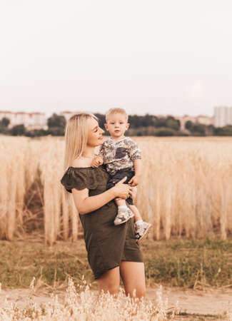 A young beautiful mother holds her young son in her arms and plays with him in the summer in nature.の写真素材