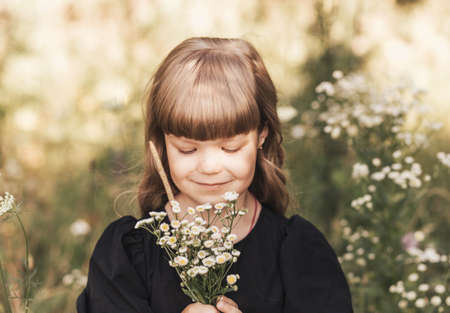 A little cute girl with long hair holds spikelets of wheat in the field in the summer. Summer. Harvest conceptの写真素材