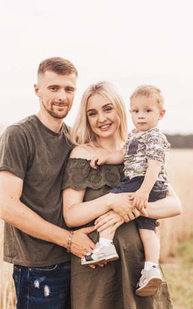 Beautiful family parents and a young son in a wheat field. Mom, Dad and Baby Together. Happy family, parents hugs their little sonの写真素材
