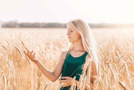 Beautiful teenage girl with long white hair walking through a wheat field on a sunny dayの写真素材
