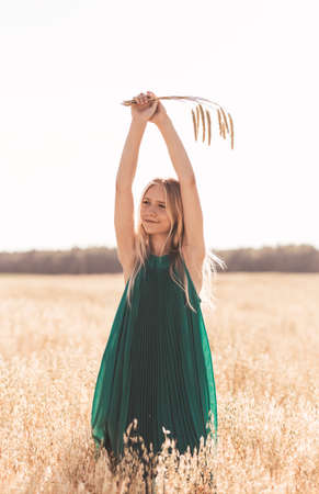 Beautiful teenage girl with long white hair walking through a wheat field on a sunny dayの写真素材