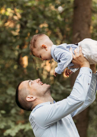 A young father holds his young son in his arms in nature in the summer. Hugs and kissesの写真素材