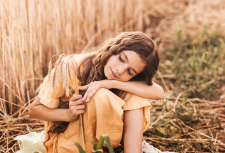 Beautiful teenage girl with long hair walking through a wheat field on a sunny day. Outdoors portrait. Schoolgirl relaxingの写真素材