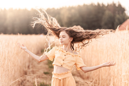 Beautiful teenage girl with long hair walking through a wheat field on a sunny day. Outdoors portrait. Schoolgirl relaxingの写真素材