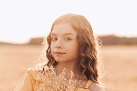 Beautiful teenage girl with long hair walking through a wheat field on a sunny day. Outdoors portrait. Schoolgirl relaxingの写真素材