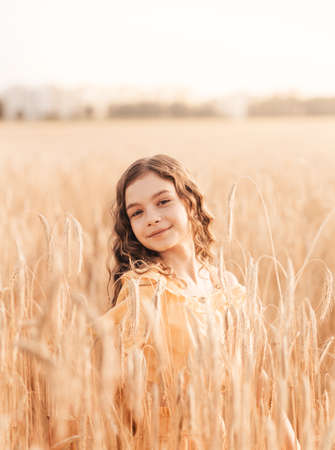 Beautiful teenage girl with long hair walking through a wheat field on a sunny day. Outdoors portrait. Schoolgirl relaxingの写真素材