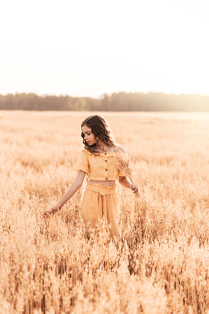 Beautiful teenage girl with long hair walking through a wheat field on a sunny day. Outdoors portrait. Schoolgirl relaxingの写真素材