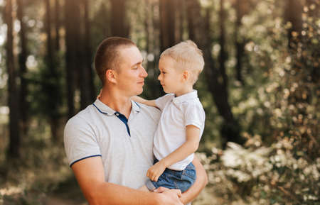 A young dad holds his young son in his arms and looks at the unlunted in nature.の写真素材