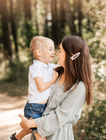 A young beautiful mother holds her young son in her arms and plays with him in the summer in nature.の写真素材