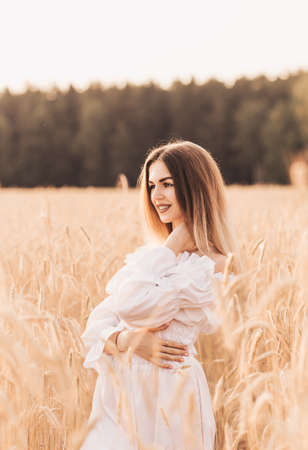 A young beautiful woman walks through a wheat field in white clothesの写真素材
