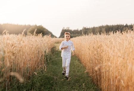 A small handsome boy blonde in a white shirt and white pants in nature in the summer. Happy childhood. Positive emotionsの写真素材