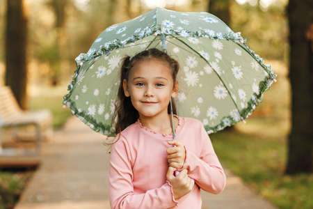 Little pretty girl sits on a bench in the park in the autumnの写真素材