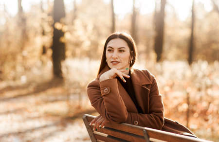 Portrait of a young woman in a coat and scarf in autumn in the parkの写真素材