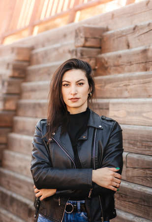 A young brunette woman in a black leather jacket in the park in the fall. Walking to the city...