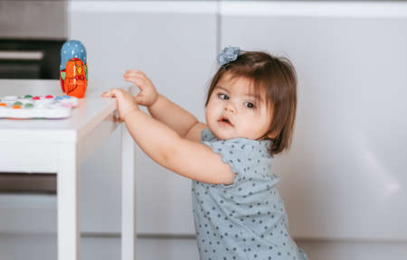 Pretty beautiful little one-year-old girl is playing with educational toy standing at the table in...