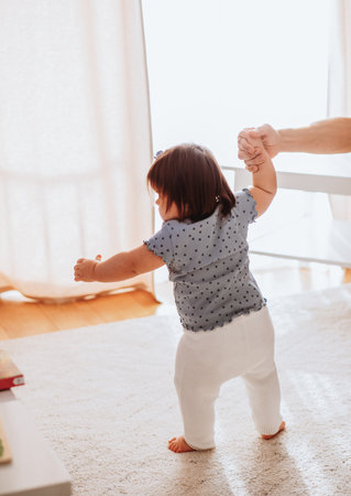 Portrait of cute small baby girl learn walking at home holding dad hands, little toddler infant...