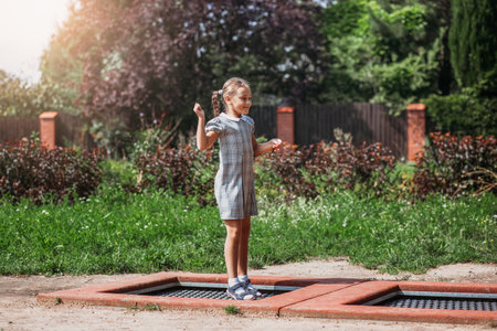 Little girl is jumping on trampoline in a park. Happy laughing kid outdoors in the yard on summer vacation. Jump highの写真素材