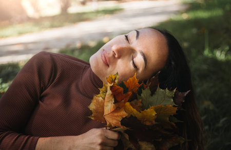 Portrait of sad beautiful young woman lying on the ground of an autumn forest with colorful maple leaves. Concept blue mondayの写真素材