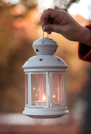 hand holds a lantern in the forest. arm holding the vintage lamp with a candle outside.