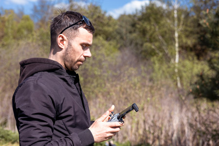 A man a drone pilot with a control panel in his hands controls a quadcopter in the field outdoor.の写真素材