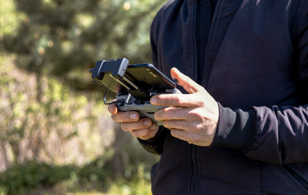 A man a drone pilot with a control panel in his hands controls a quadcopter in the field outdoor.