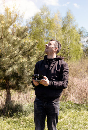 A man a drone pilot with a control panel in his hands controls a quadcopter in the field outdoor.