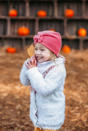 smiling happy little child girl in coat holding autumn leaves, having fun in fall forestの写真素材