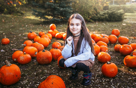 Autumn harvest of pumpkins. Child and orange pumpkin at farm market or seasonal festival. Cute little girl playing among pumpkins. Thanksgiving holiday season and Halloween.の写真素材