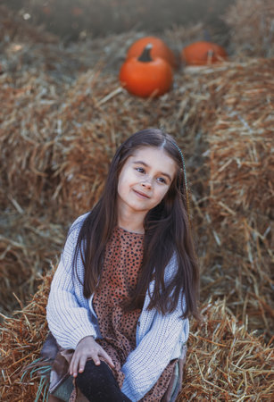 Autumn harvest of pumpkins. Child and orange pumpkin at farm market or seasonal festival. Cute little girl playing among pumpkins. Thanksgiving holiday season and Halloween.の写真素材