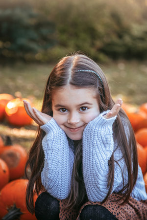 Autumn harvest of pumpkins. Child and orange pumpkin at farm market or seasonal festival. Cute little girl playing among pumpkins. Thanksgiving holiday season and Halloween.の写真素材