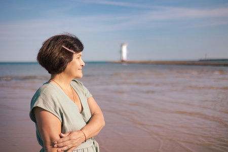 Happy senior woman in long dress walking on tropical island beach at summer sunset. Elderly retired woman relax and enjoy outdoor lifestyle activity in summer beach holiday travel vacation.の写真素材