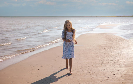 Little girl with lond hair in beautiful dress running on sea beach during summer holiday.Child playing on ocean beach. Sea vacation for family with kids.の写真素材