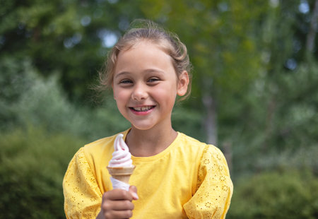 Cute laughing child little girl eats ice cream on a hot day. Ice cream in a waffle cone. A happy and contented child at summer.の写真素材