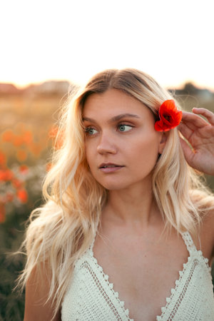 Portrait of young blonde woman with red poppy flower at sunset in summerの写真素材