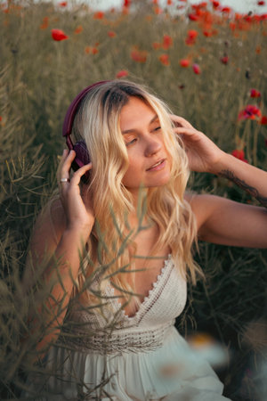 Young beautiful blonde woman in headphones listening to music outdoors in summerの写真素材