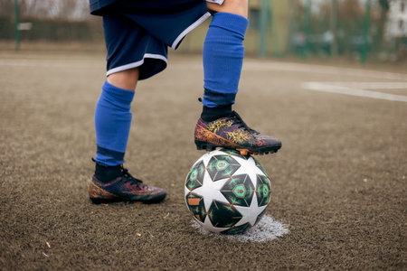 Close-up of a child footballerâ€™s foot in a soccer cleat resting on a ball on a football field