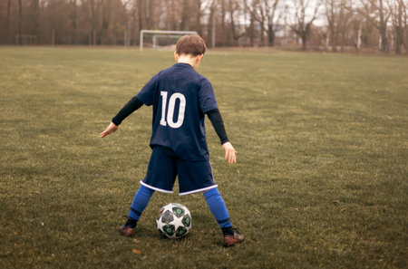 A young boy football player playing soccer near the goalposts on a football field