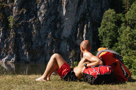 bearded man with naked torso is resting near mountain rivere after road or hike. lying on his backpack. summer outdoor activities.の写真素材
