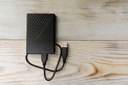Portable hard drive for backing up various files on wood background. Top view